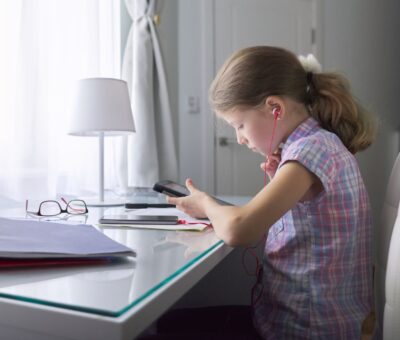 Dziewczynka przy biurku czyta coś w telefonie